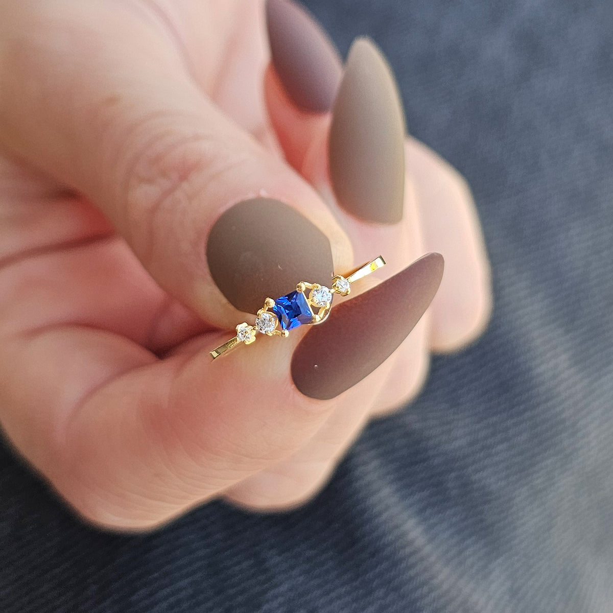Gold blue-stone princess ring on raised hand