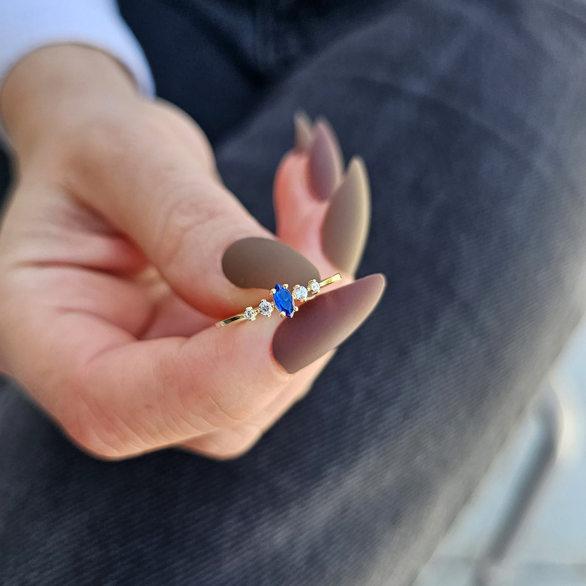 Gold blue-stone marquise ring on raised hand