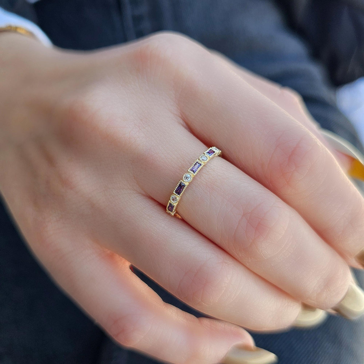 Gold purple-stone baguette ring on raised hand