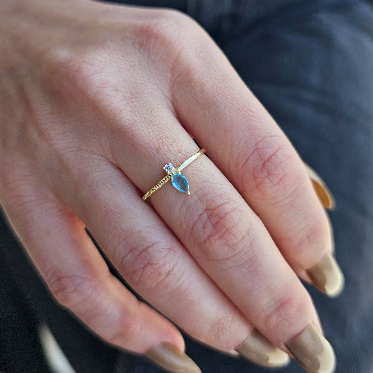 Gold aqua-blue-stone pear ring worn on hand, close-up