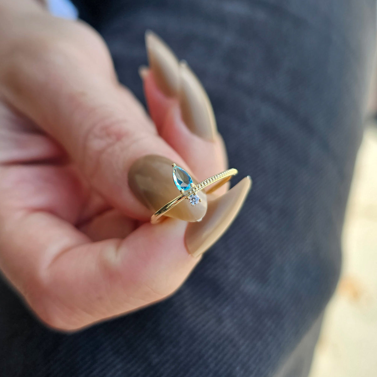 Gold aqua-blue-stone pear ring on raised hand