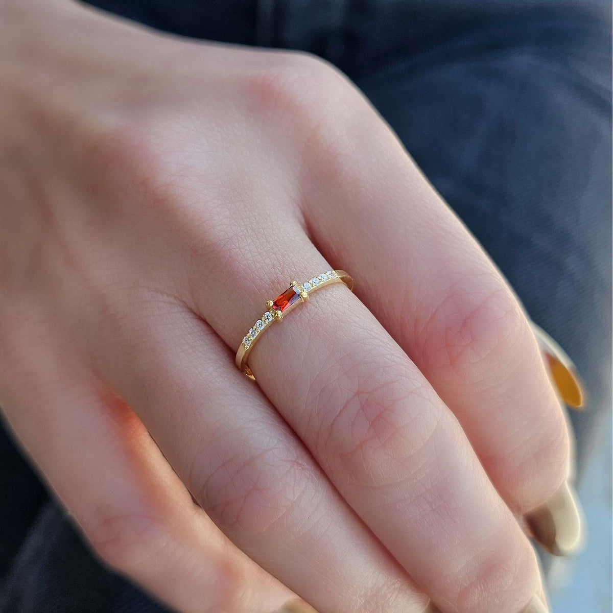 Gold dark-red-stone baguette ring on raised hand