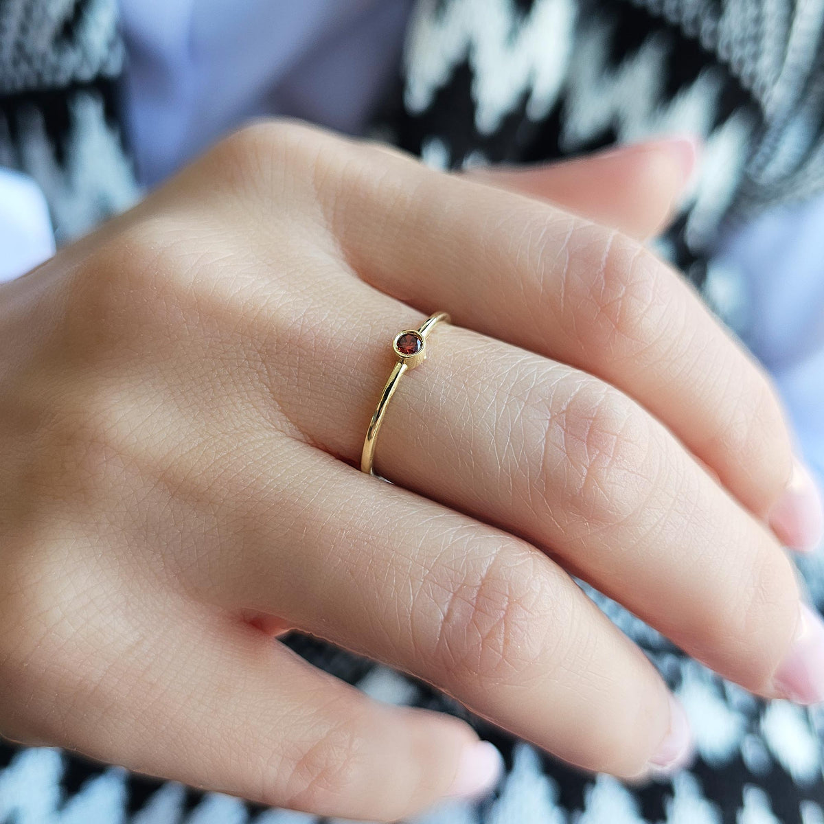 Gold dark-red-stone bezel solitaire ring on raised hand