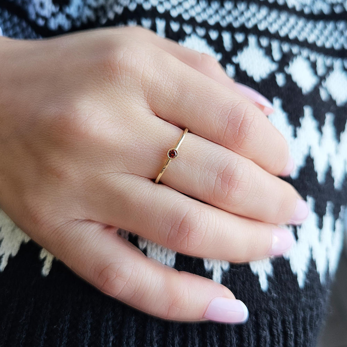 Gold dark-red-stone bezel solitaire ring worn on hand, side view