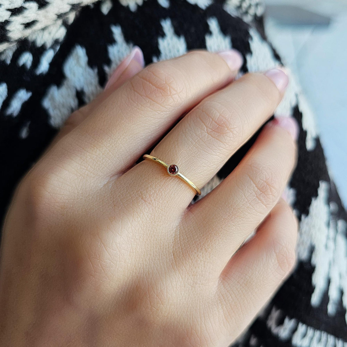 Gold dark-red-stone bezel solitaire ring worn on hand, close-up