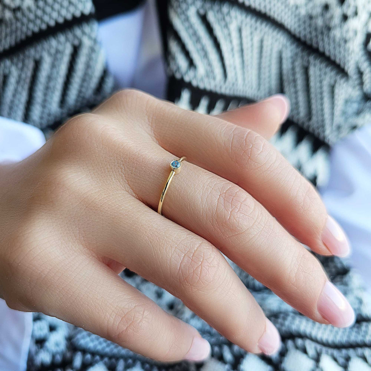Gold light-blue-stone bezel solitaire ring worn on hand, side view