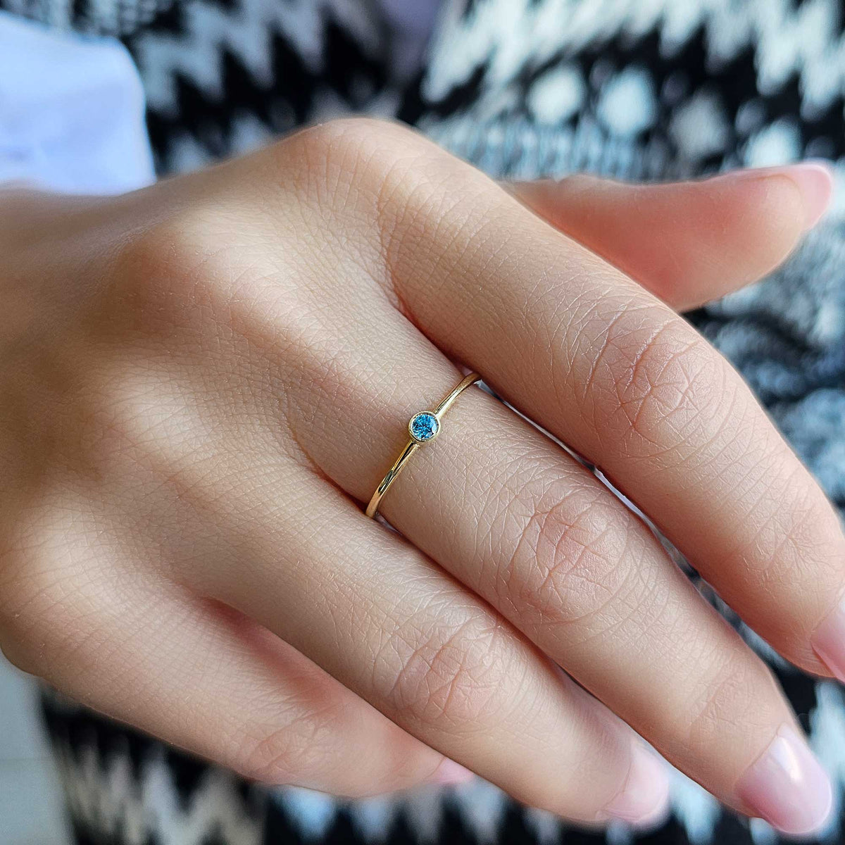 Gold light-blue-stone bezel solitaire ring worn on hand