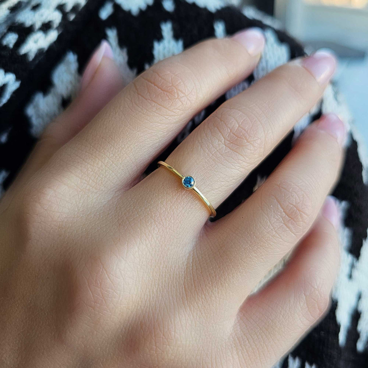Gold light-blue-stone bezel solitaire ring worn on hand, close-up