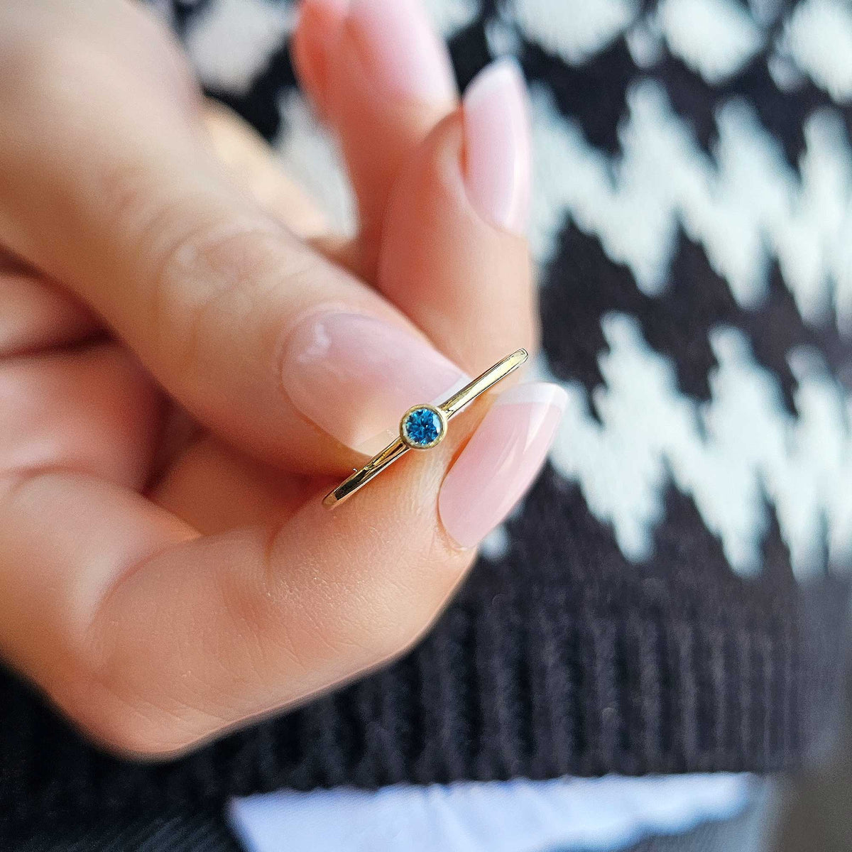 Gold light-blue-stone bezel solitaire ring on raised hand