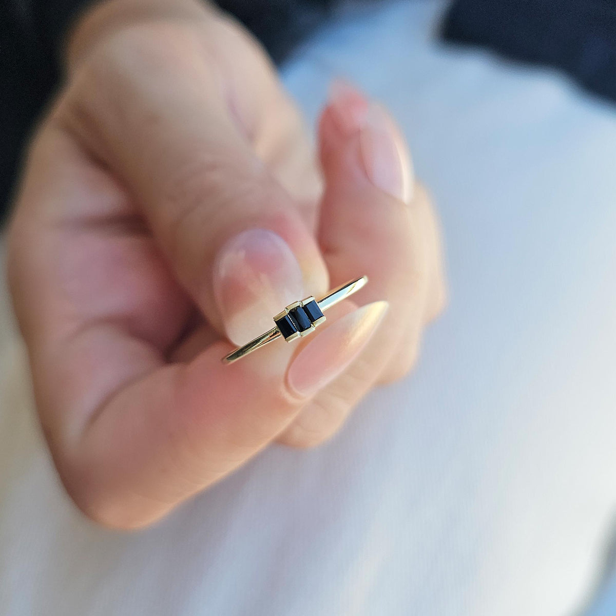 Gold black onyx three-baguette ring on raised hand