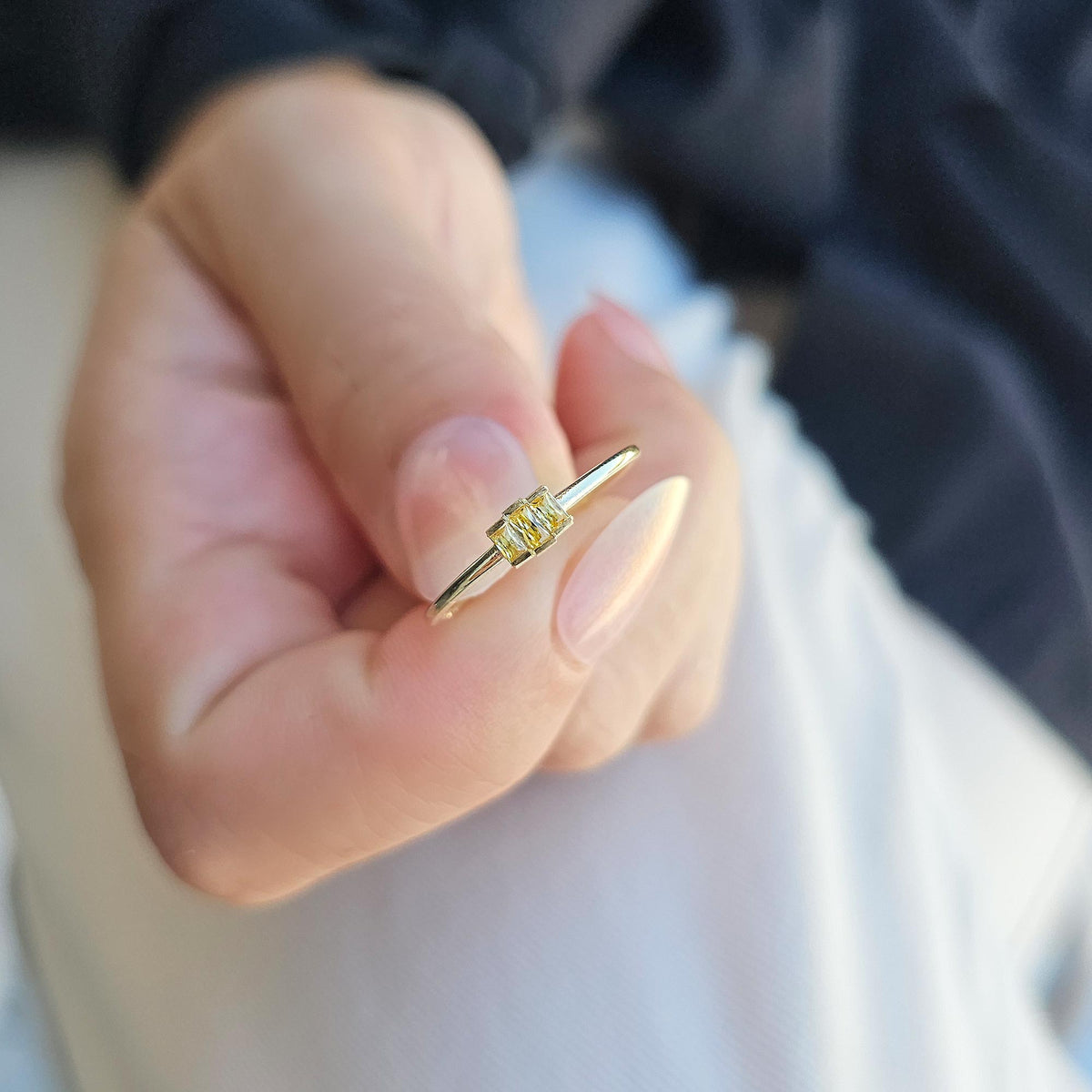 Gold yellow-stone three-baguette ring on raised hand
