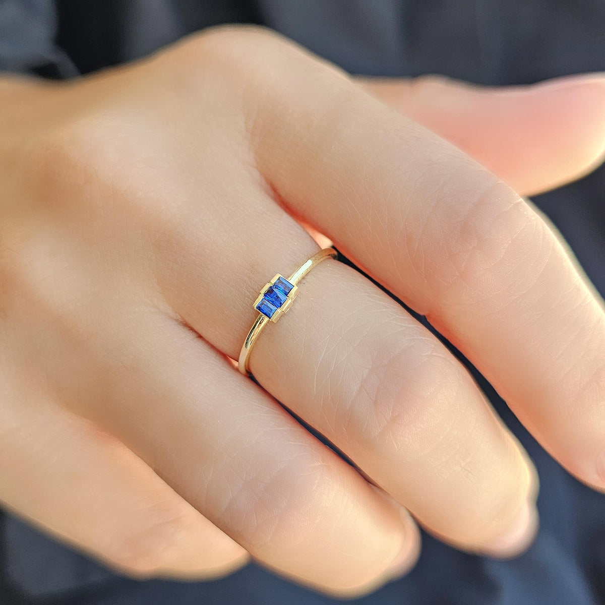 Gold blue-stone three-baguette ring worn on hand, side view
