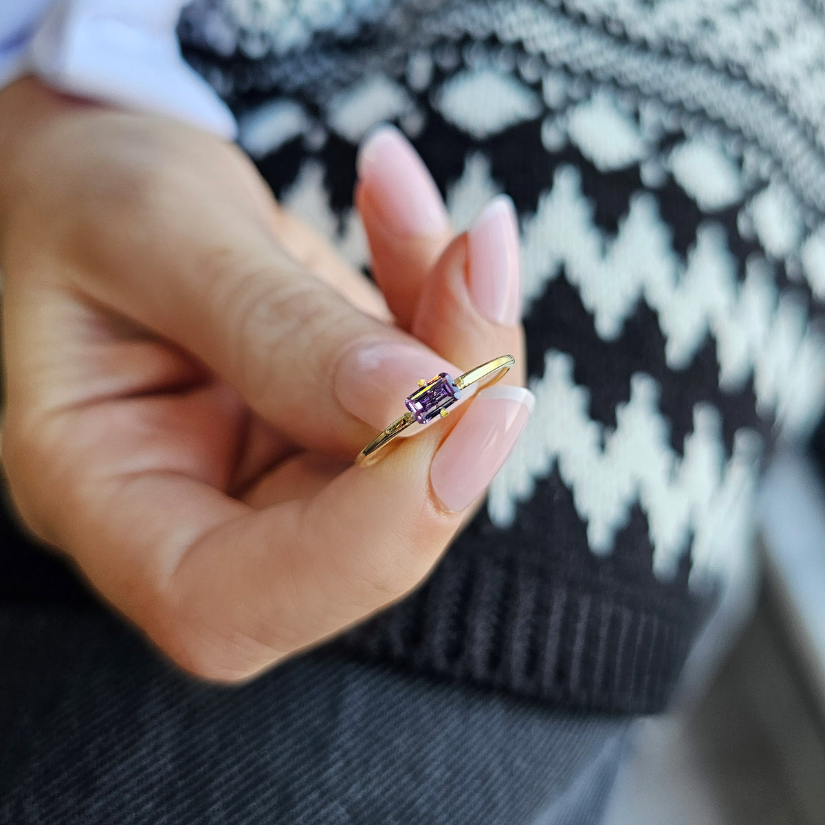 Gold purple-stone baguette solitaire ring on raised hand
