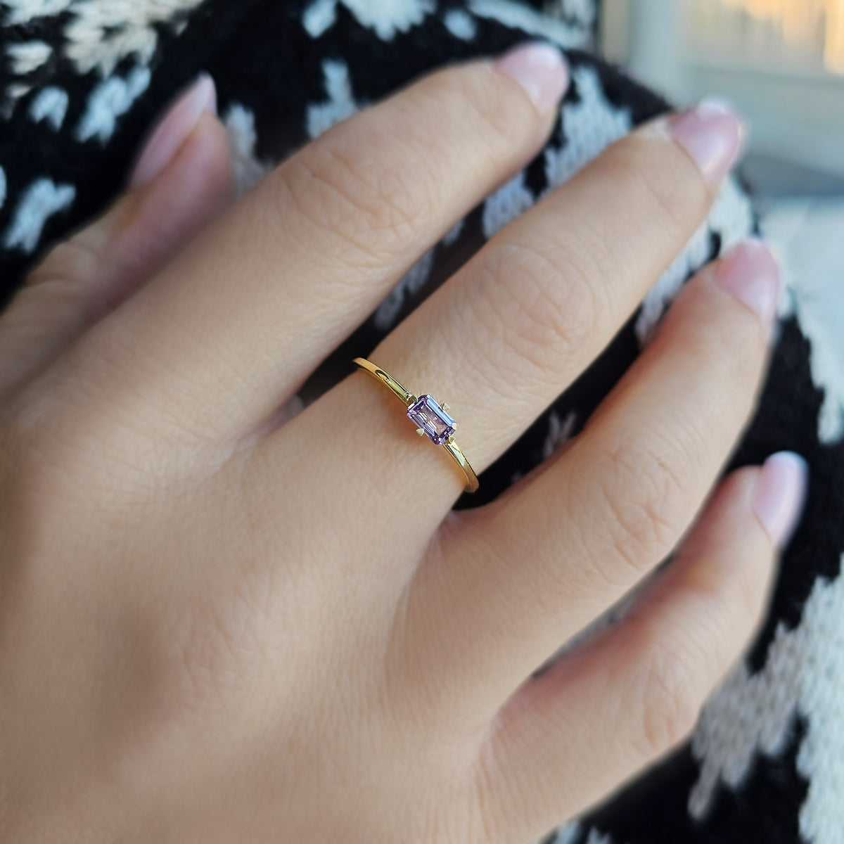 Gold purple-stone baguette solitaire ring worn on hand, close-up