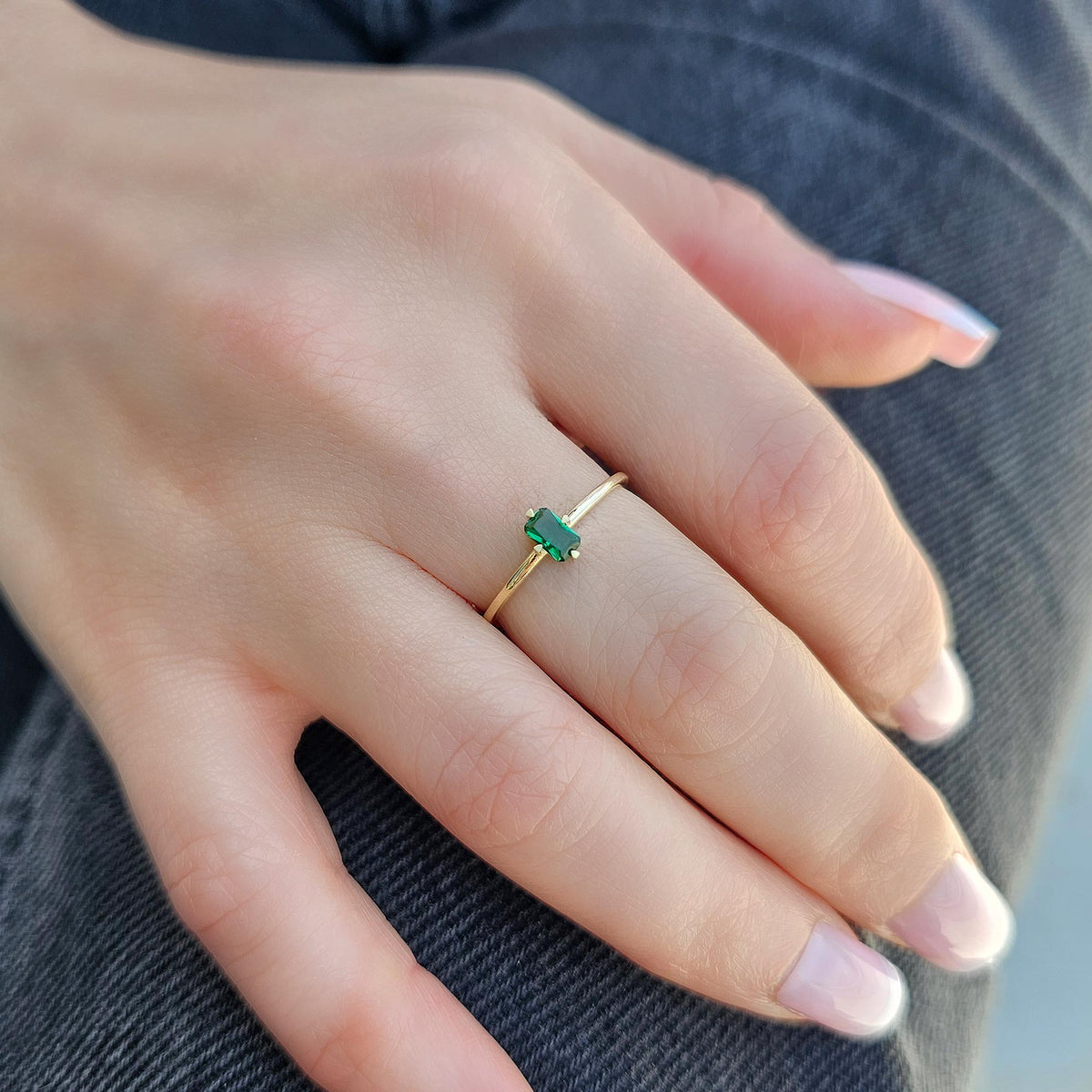 Gold green-stone baguette solitaire ring on raised hand