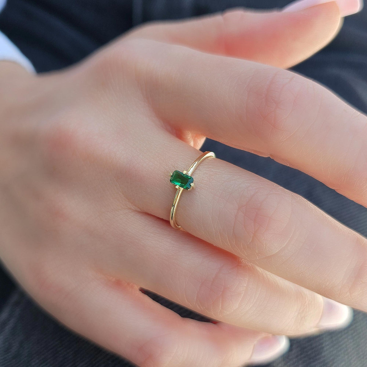 Gold green-stone baguette solitaire ring worn on hand, side view