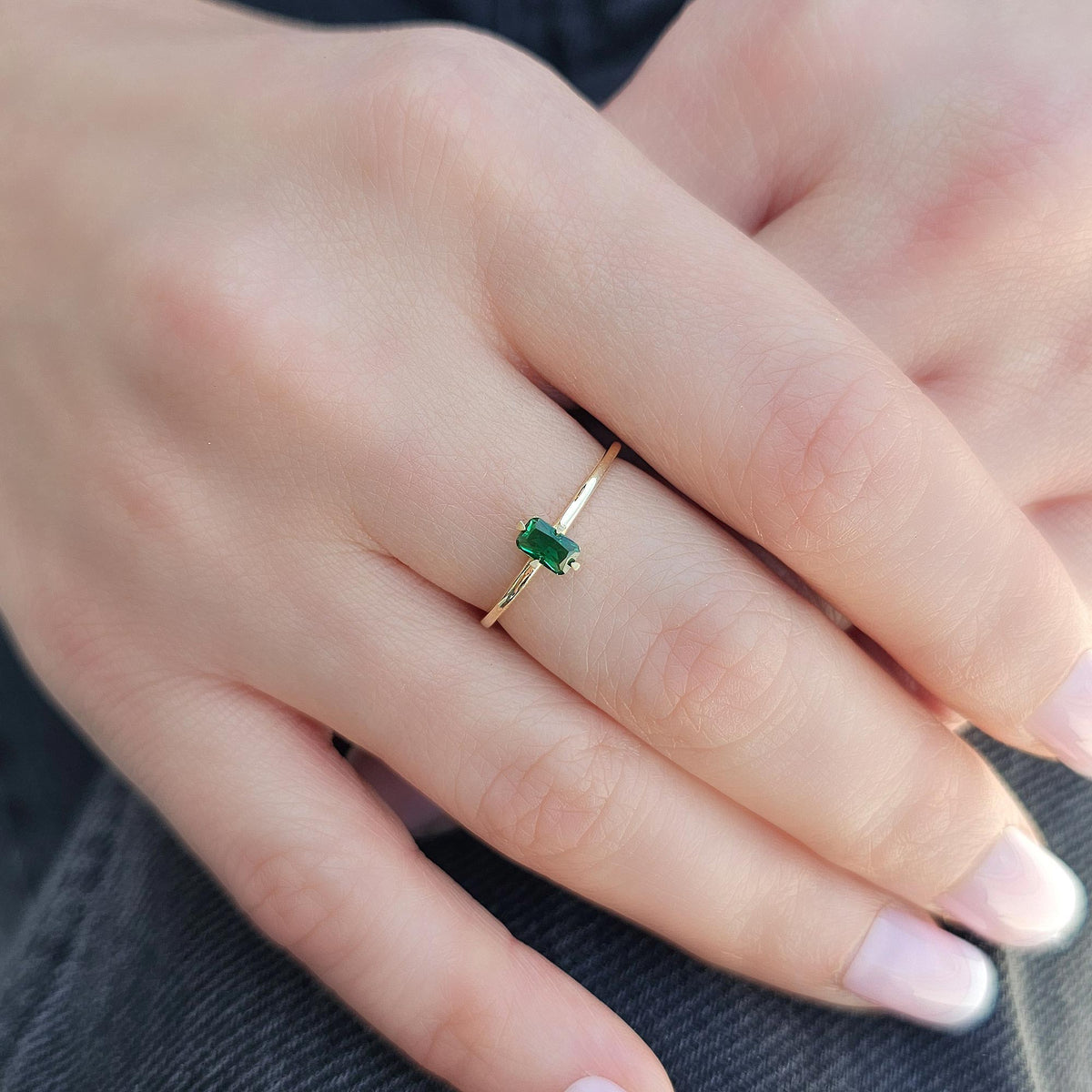 Gold green-stone baguette solitaire ring worn on hand