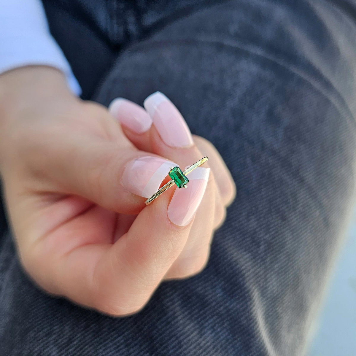 Gold green-stone baguette solitaire ring worn on hand, close-up