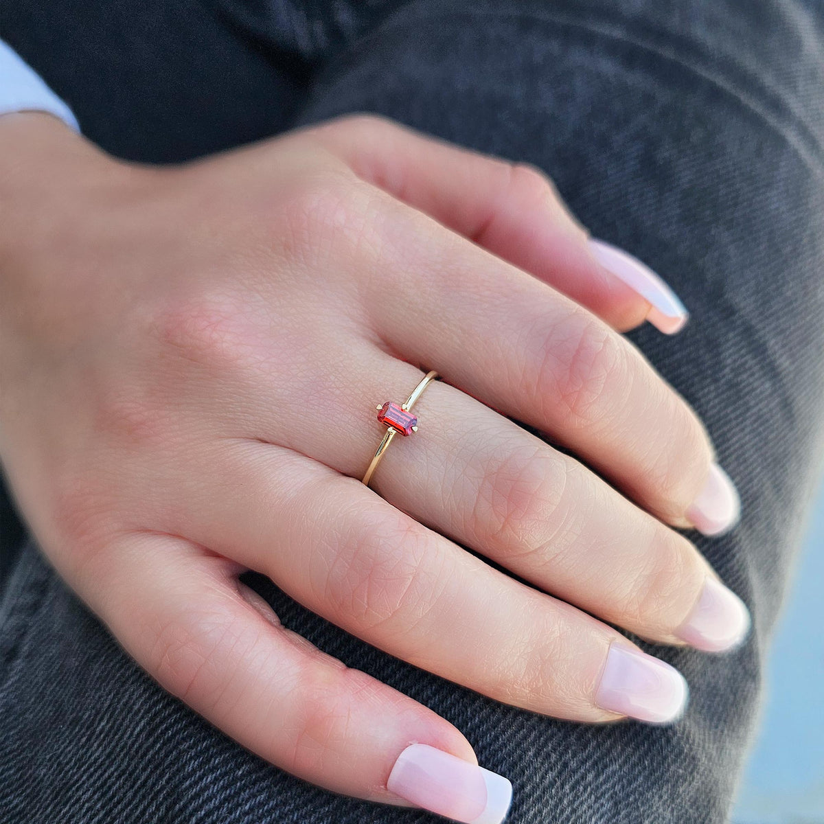 Gold dark-red-stone baguette solitaire ring worn on hand