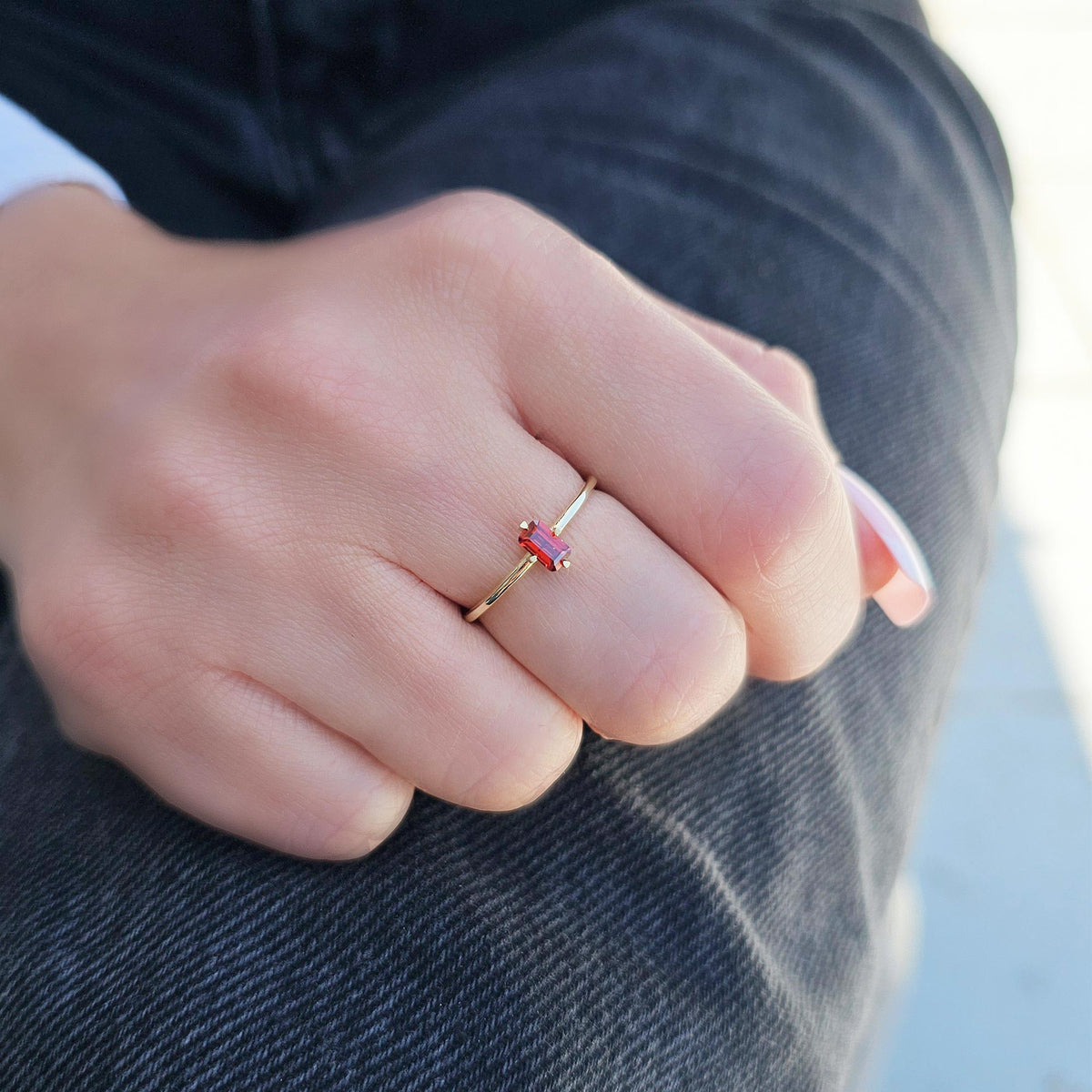 Gold dark-red-stone baguette solitaire ring worn on hand, close-up