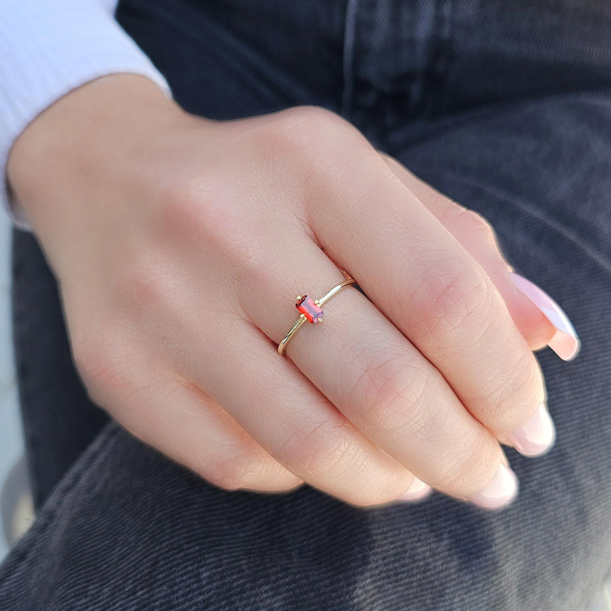 Gold dark-red-stone baguette solitaire ring worn on hand, side view
