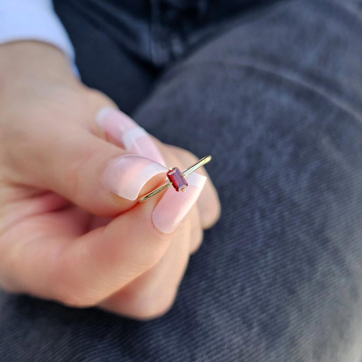 Gold dark-red-stone baguette solitaire ring on raised hand