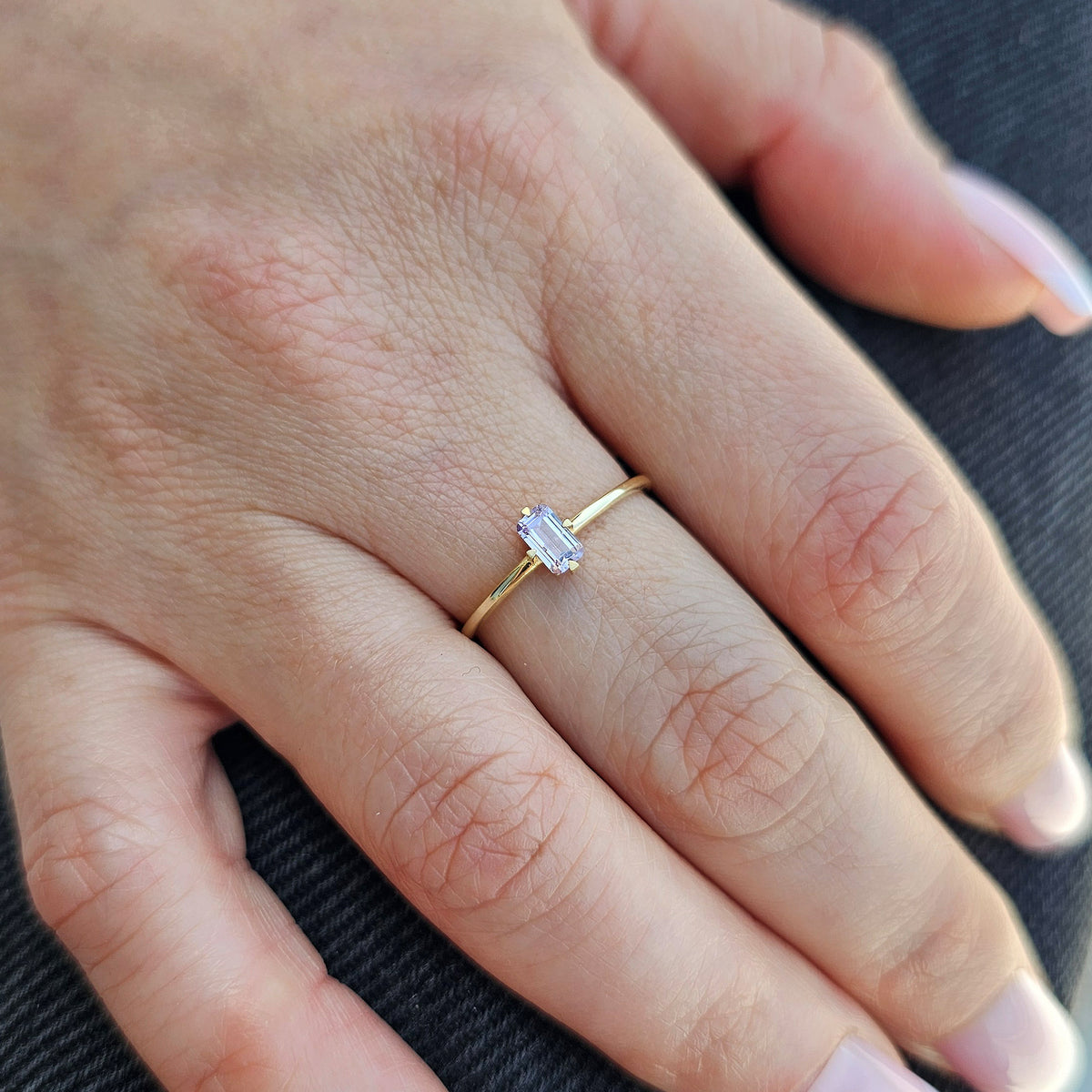 Gold lavender-stone baguette solitaire ring worn on hand, close-up
