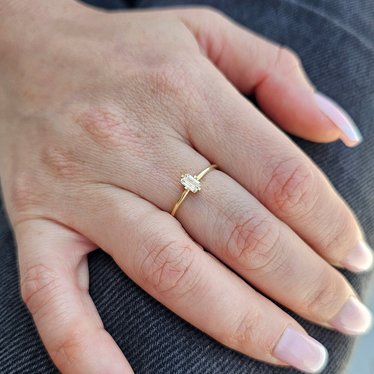 Gold lemon-yellow-stone baguette solitaire ring on raised hand