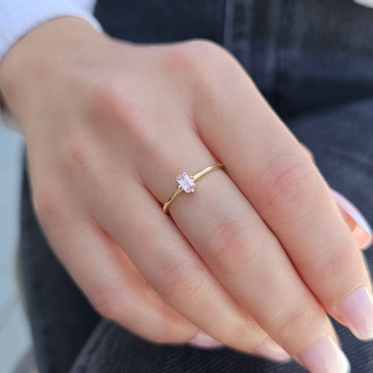 Gold pink-stone baguette solitaire ring worn on hand, close-up