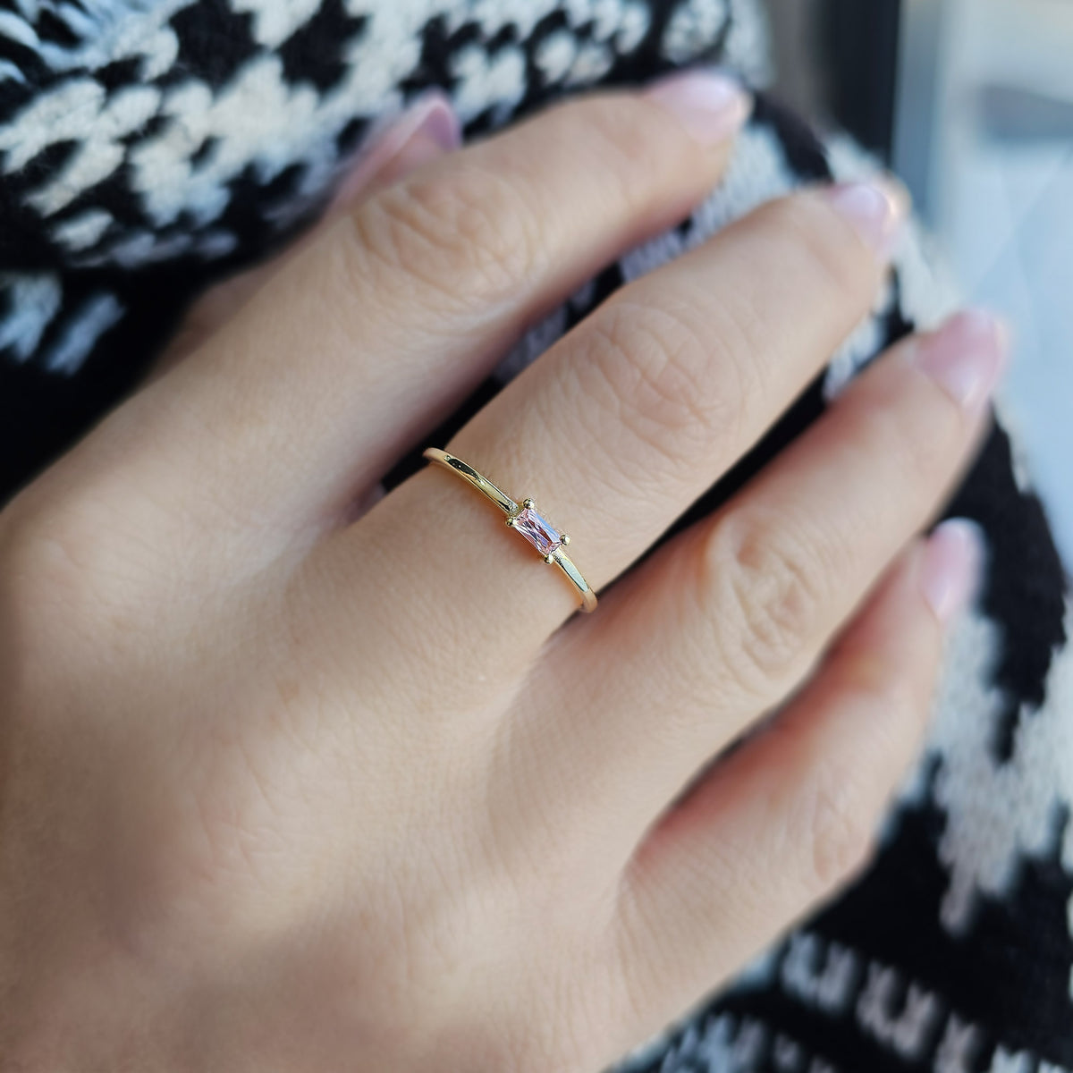 Gold pink-stone baguette solitaire ring on raised hand