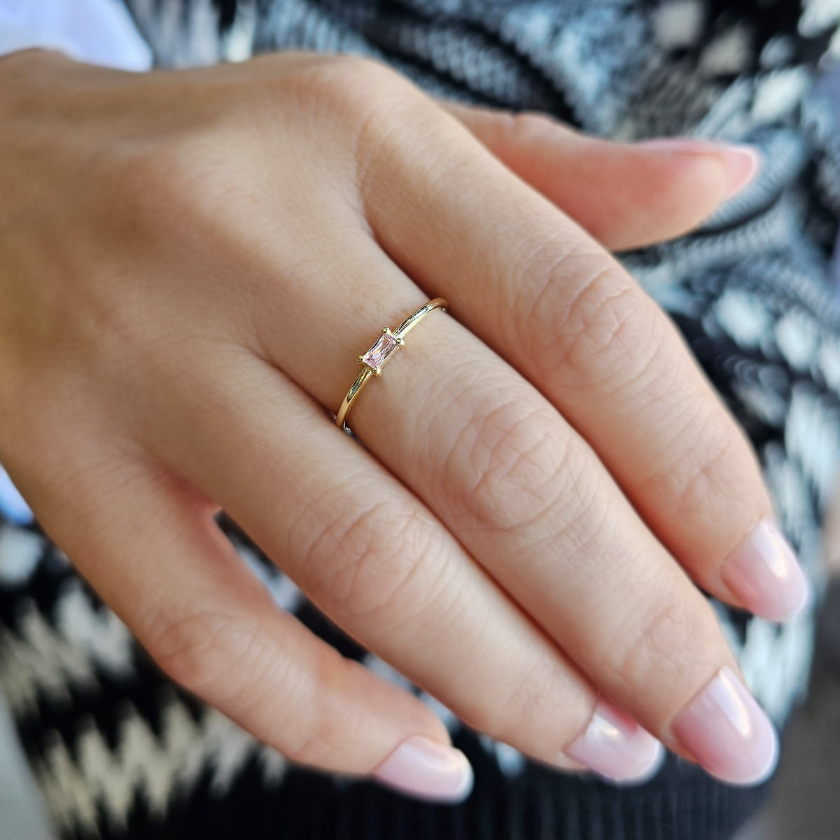 Gold pink-stone baguette solitaire ring worn on hand, close-up