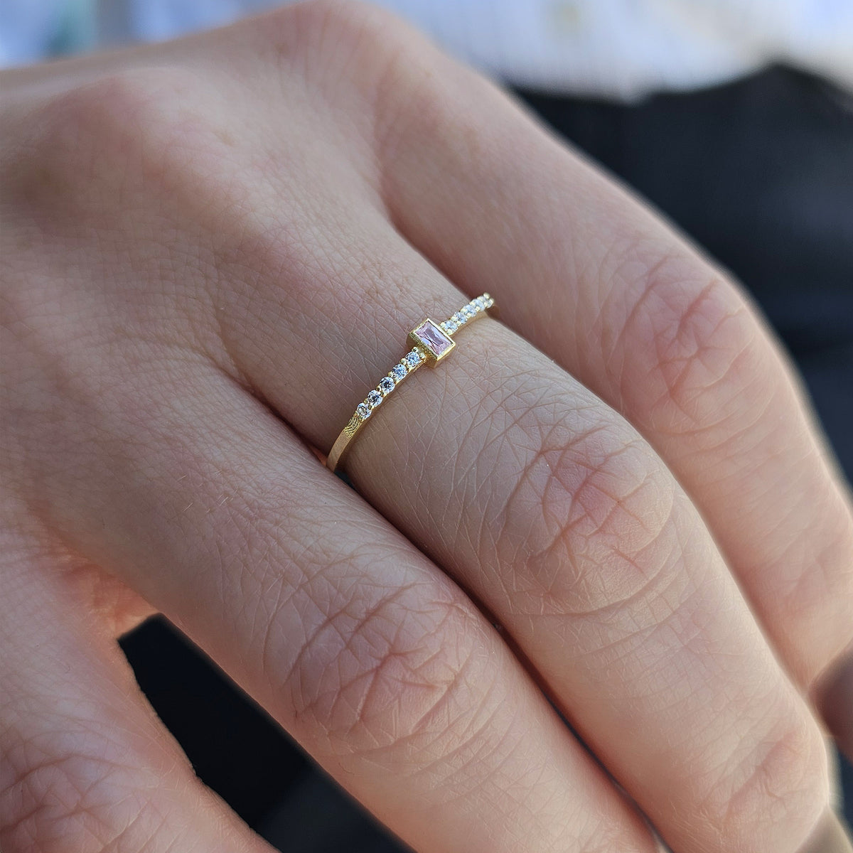 Gold pink-stone baguette ring on raised hand
