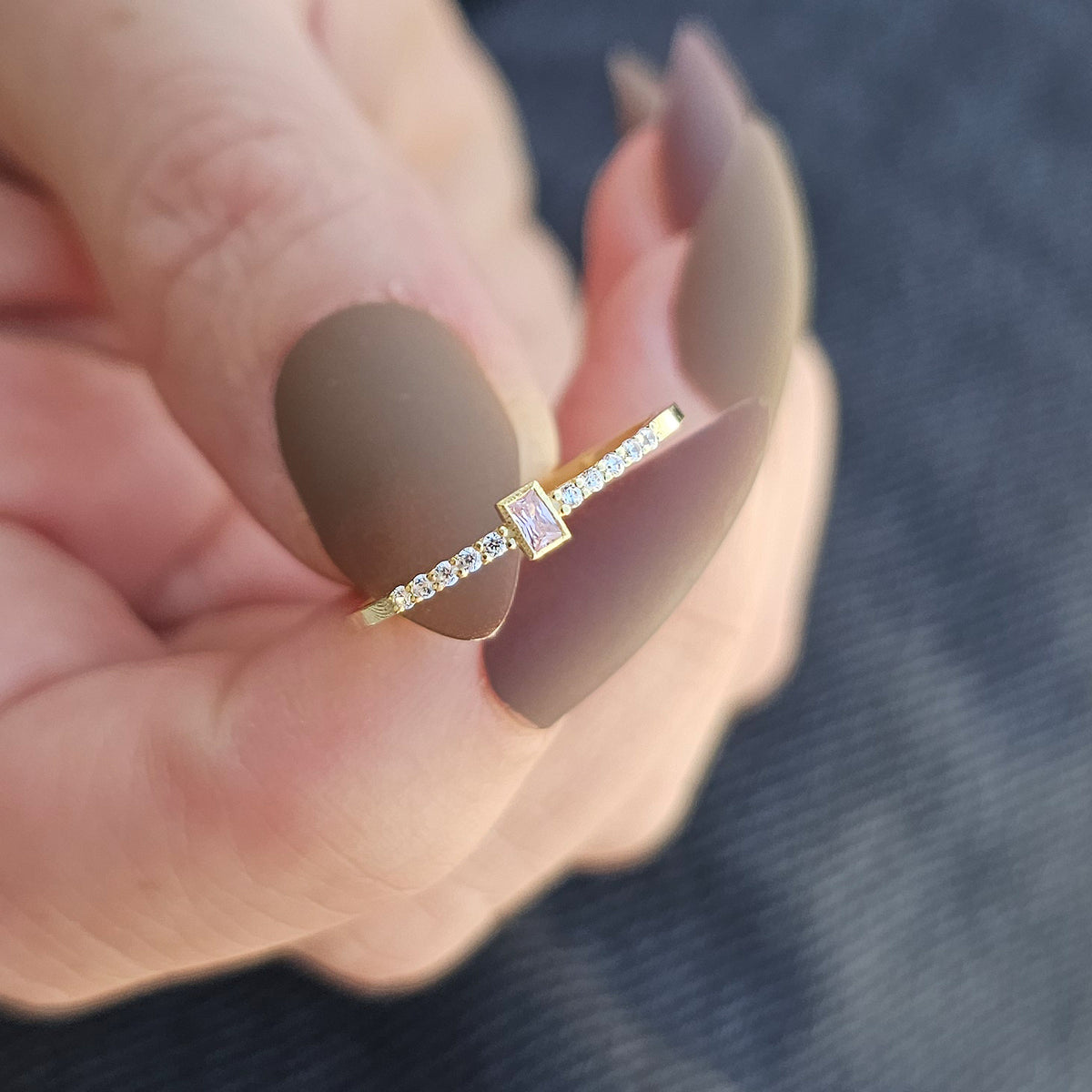 Gold pink-stone baguette ring worn on hand, close-up