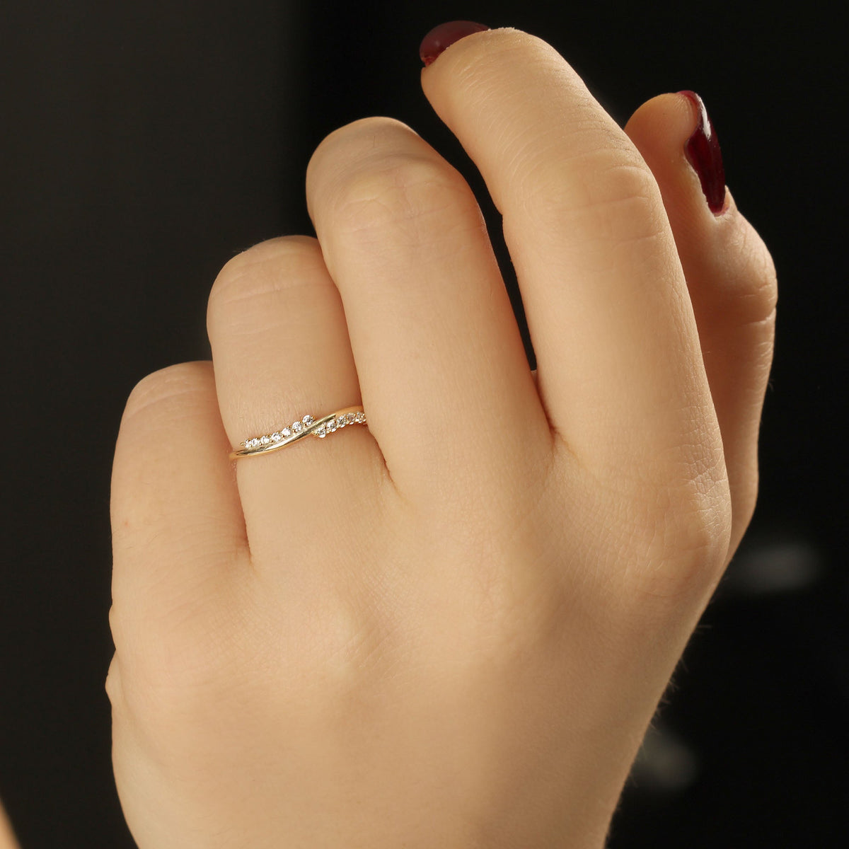 14K gold curved wave diamond ring worn on hand, close-up
