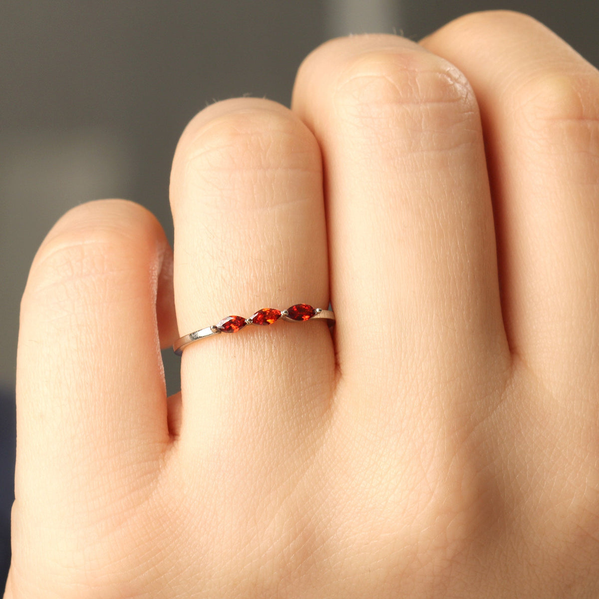 18K gold three stone marquise ring with orange-red marquise stones on raised hand